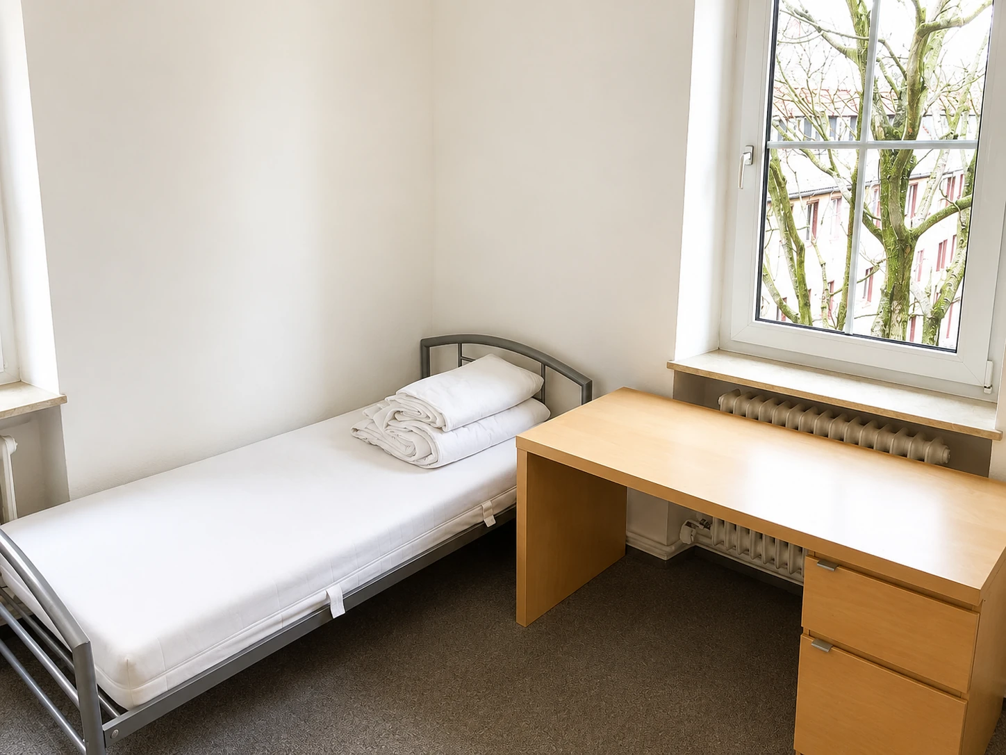 Studentenzimmer mit Bett, Schreibtisch und zwei Fenstern