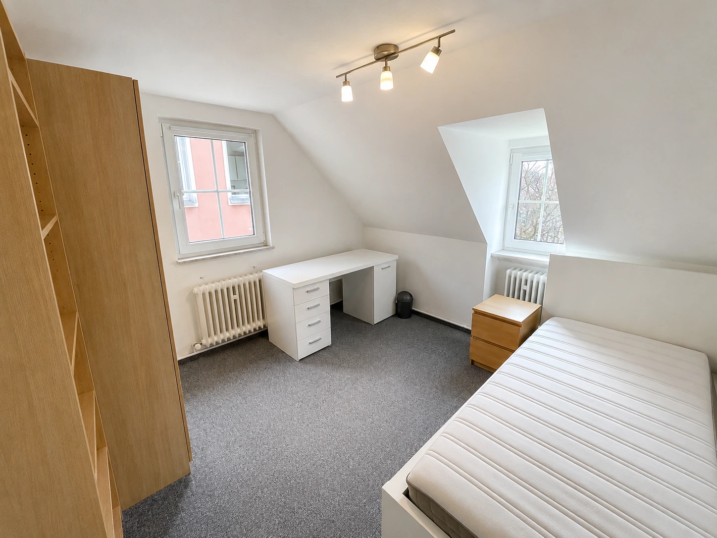 Studentenzimmer mit Dachschräge, Schrank, Schreibtisch und Bett